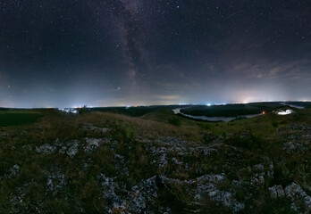 Milk Way night sky over hills and Dniester river. Night nature landscape. City lights on background. Ukraine