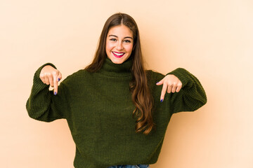 Young caucasian woman isolated en beige background points down with fingers, positive feeling.