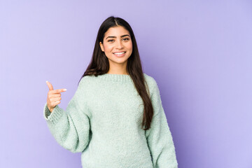 Wall Mural - Young indian woman isolated on purple background person pointing by hand to a shirt copy space, proud and confident