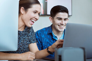 Young man and woman co-workers gathered around laptop computer laughing 