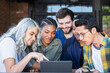 © SuperStock - Group of young people working on a digital tablet at an outdoor cafe.