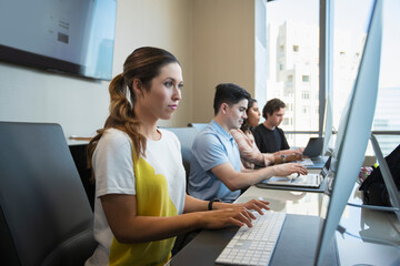 Young woman using computer in office typing on keyboard, co-workers working in background 