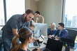 © SuperStock - worker in office conference room providing tech support to colleague working on laptop, co-workers working in background