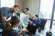 © SuperStock - worker in office conference room providing tech support to colleague working on laptop, co-workers working in background