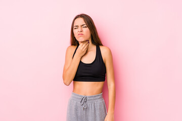 Wall Mural - Young caucasian fitness woman posing in a pink background suffers pain in throat due a virus or infection.