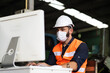 © NVB Stocker - Young caucasian engineering man worker working on digital tablet computer at manufacturing. Worker man wearing face mask prevent covid-19 virus and protective hard hat.