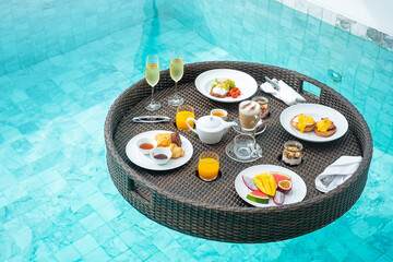 Floating Breakfast tray in swimming pool at luxury hotel or tropical resort villa, fruits; mango, watermelon dragon and passion fruit, food, bread, coffee, tea, wine and orange juice. Exotic summer