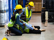 © NVB Stocker - First Aid. Workers man and woman taking care female colleague lying on the floor in a warehouse. safety first and  insurance concept