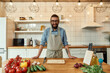 © Svitlana - Young man, Italian cook in apron smiling at camera while preparing healthy meal with vegetables in the kitchen. Cooking at home concept