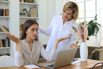 Two female collegues working with laptop and discussing new project.