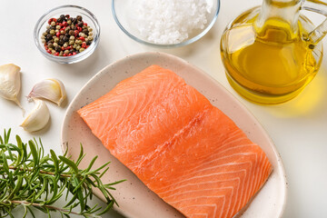 Raw chilled salmon fillet on a plate, fresh rosemary, garlic, pepper, sea salt and olive oil on a kitchen table. Healthy eating, seafood recipe ingredient and organic omega 3 concepts.