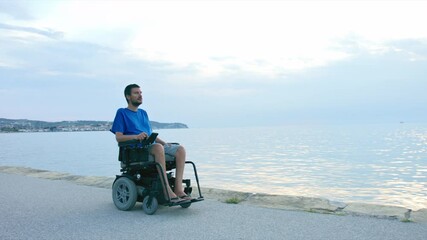 Wall Mural - Man on wheelchair near sea looking at sunset.
