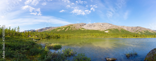 Mountain valley lake panorama against the background of a mountain range and blue sky with white clouds