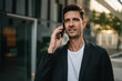 © iana_kolesnikova - Portrait of happy businessman talking on smartphone outdoors near office buildings, Successful employer making deal on smartphone with business partner walking in the city center