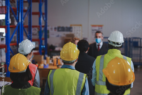 Manager and warehouse work team discuss preventive measures, spaced distance, wear anti-virus masks, workers in warehouse concept.