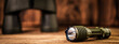 Banner detail close up of army - hunting binocular and flashlight on a blurred wooden background. 