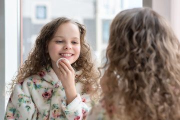 Poster - Portrait of beautiful little girl enjoying skincare procedures front of the mirror in her home bathroom.