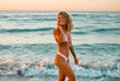 © Valerii Apetroaiei - Attractive Caucasian woman in bikini swimsuit strolls on the beach at sunrise enjoying the sound of the waves.