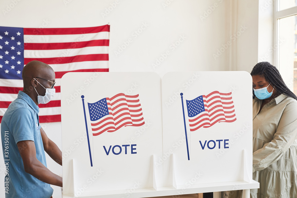 Side view portrait of two African-American people wearing masks standing in voting booths opposite each other on post-pandemic election day, copy space - obrazy, fototapety, plakaty 