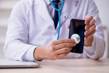 Young male doctor with stethoscope repairing computer