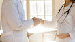 © fizkes - Close up two doctors colleagues shaking hands, greeting, celebrating success, young woman and man wearing white uniform standing in office in hospital, medical staff teamwork concept