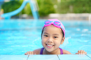 Asian child cute or kid girl wear swimming suit and goggles on swimming pool and smile with happy fun in water park for learn and training swim or refreshing and relax with exercise on summer holiday