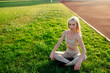 © Maria - Beautiful young blonde woman in sportswear sits on the grass in the stadium before training