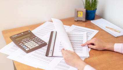 female accountant or banker making calculations sitting at office table with documents with tables on desk pointing at digits on documents. Savings, finances and economy concept