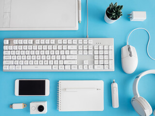 Poster - top view of office desk table with notebook, plastic plant, smartphone and keyboard on blue table background, graphic designer.