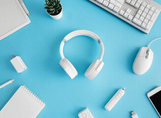 Poster - top view of office desk table with notebook, plastic plant, smartphone and keyboard on blue table background, graphic designer.