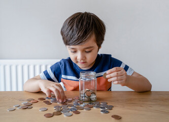 school kid putting money coins into clear jar, child counting his saving money, young boy holding co