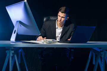 Poster - Successful businessman. Earnings on the Internet. Remote work. A man is sitting at a table with two computers. In front of the person are bundles of money. Successful entrepreneur.