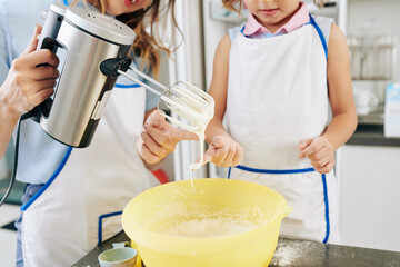 Wall Mural - Cropped image of mother and daughter tasting sweet cream they made for cake