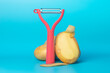 Red vegetable peeler and potatoes on a blue background