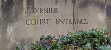 Weathered Stone Slab Sign With The Words Juvenile Court Entrance Engraved Into It With Foliage At The Bottom Outside The Department Of Justice Courthouse Where Juveniles Are Tried. 