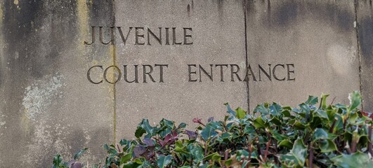 weathered stone slab sign with the words juvenile court entrance engraved into it with foliage at th