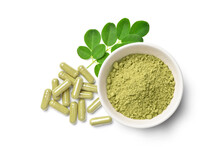 Flat Lay (top View) Of Finely Ground Dried  Moringa Leaves In White Bowl With Powder Capsules And  Fresh Green  Leaves Isolated On White Background.