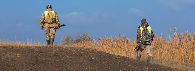 Hunters man in rural field with shotgun and backpack during hunting season