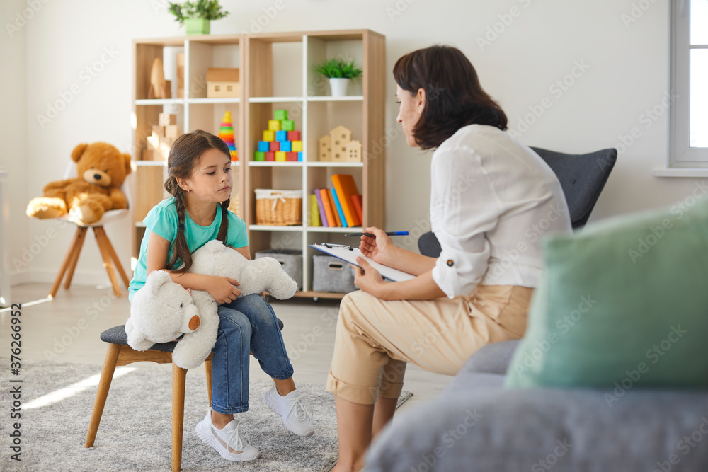 Little girl sharing her concerns with supportive child psychologist during therapy session in - obrazy, fototapety, plakaty 