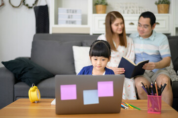 Wall Mural - Asian Happy daughter are using laptop for studying online via internet while parent sitting on couch at home. E-learning Concept