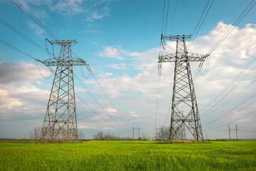 High voltage lines and power pylons in a flat and green agricultural landscape on a sunny day with clouds in the blue sky. Cloudy and rainy. Wheat is growing