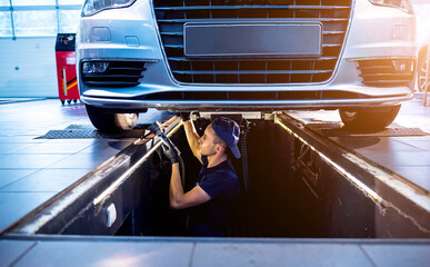 Wall Mural - Car mechanic examining car suspension of lifted automobile at service station