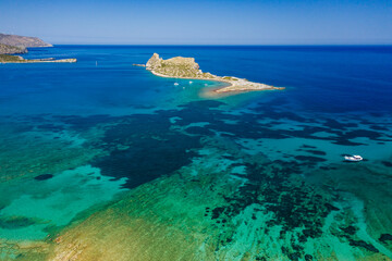 Aerial view of boats in a crystal clear blue ocean next to a small island (Kolokitha, Crete, Greece)