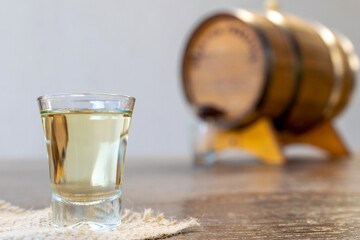 glass of high quality distilled alcohol and defocused old oak barrel in the background. Cachaça is a typical drink from Brazil, also known as cognac.