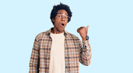 Handsome african american man with afro hair wearing casual clothes and glasses surprised pointing with hand finger to the side, open mouth amazed expression.