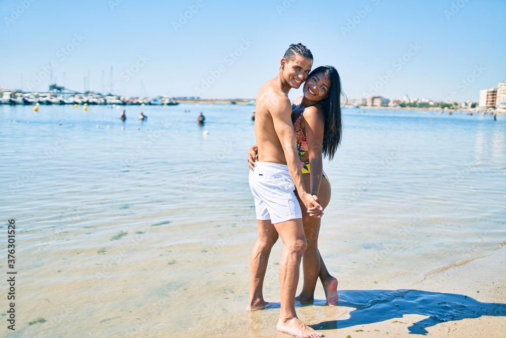 Young latin couple wearing swimwear  smiling happy and dancing at the beach.