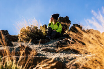 Woman relaxing sit down on the ground after a trekking excursion - concept of travel and outdoor leisure sport hike activity with caucasian people enjoying the nature - blue sky background