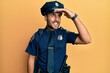 © Krakenimages.com - Handsome hispanic man wearing police uniform very happy and smiling looking far away with hand over head. searching concept.