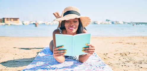 Young african american woman on vacation laying on the towel reading book at the beach