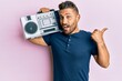 © Krakenimages.com - Handsome man with beard holding boombox, listening to music pointing thumb up to the side smiling happy with open mouth